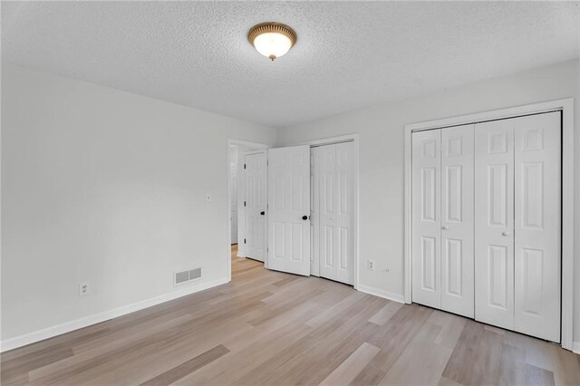 unfurnished bedroom with light wood-type flooring, a textured ceiling, and two closets