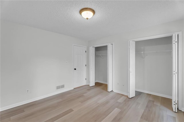 unfurnished bedroom featuring a textured ceiling, light hardwood / wood-style floors, and multiple closets