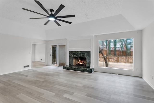 unfurnished living room with a raised ceiling, a premium fireplace, ceiling fan, and light hardwood / wood-style floors