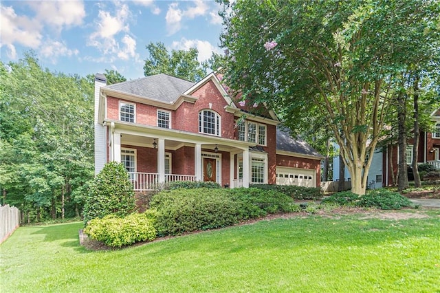 colonial home featuring a porch, a garage, and a front yard