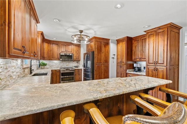 kitchen featuring decorative backsplash, appliances with stainless steel finishes, a sink, light stone countertops, and a peninsula