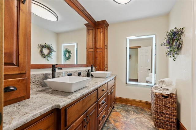 bathroom with double vanity, stone finish flooring, baseboards, and a sink