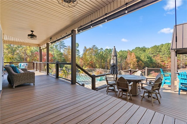 wooden terrace with outdoor dining space, ceiling fan, and a wooded view