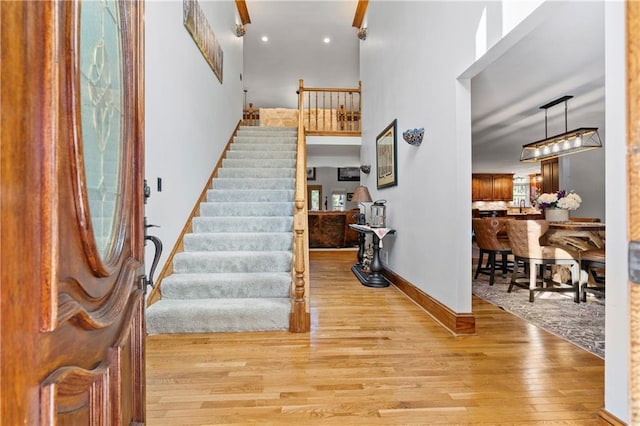 foyer featuring stairs, light wood-type flooring, a towering ceiling, and baseboards