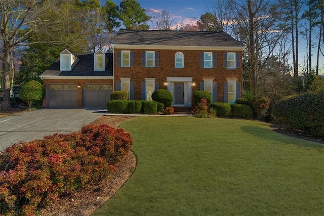 colonial-style house featuring brick siding, a lawn, driveway, and an attached garage