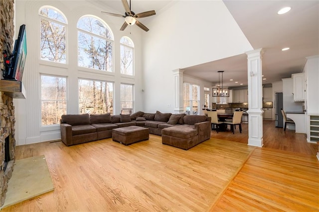 1105 River Laurel Dr, Suwanee, GA 30024 - living room featuring ornate columns, light wood-style floors, a fireplace, ceiling fan, and a towering ceiling
