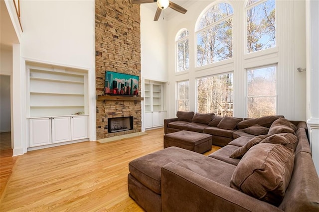 1105 River Laurel Dr, Suwanee, GA 30024 - living room featuring a towering ceiling, a stone fireplace, a ceiling fan, light wood-style floors, and built in shelves