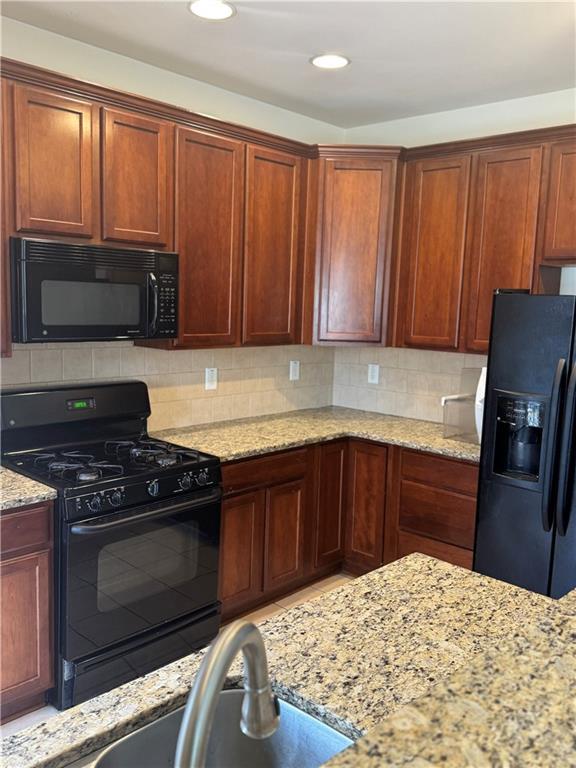 kitchen featuring sink, decorative backsplash, light stone counters, and black appliances