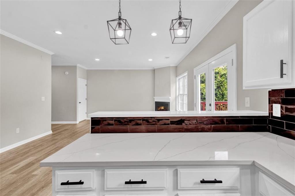 583 Whitaker St, Atlanta, GA 30318 - kitchen with a lit fireplace, crown molding, light wood-style floors, white cabinetry, and hanging light fixtures