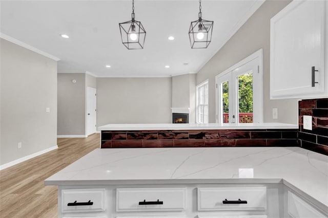 583 Whitaker St, Atlanta, GA 30318 - kitchen with a lit fireplace, crown molding, light wood-style floors, white cabinetry, and hanging light fixtures