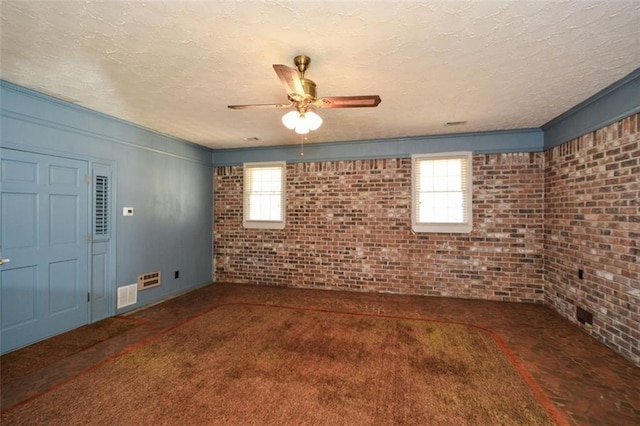 empty room featuring a ceiling fan, visible vents, brick wall, and a textured ceiling