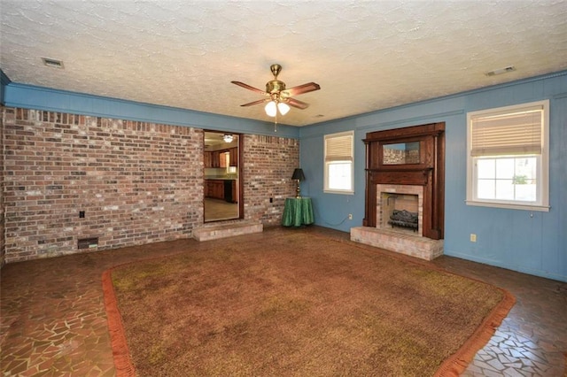 unfurnished living room featuring brick wall, a fireplace with raised hearth, a wealth of natural light, and a textured ceiling