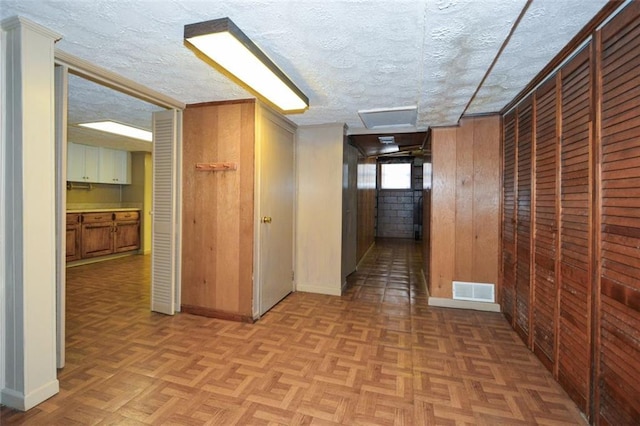 hallway with visible vents, wood walls, a textured ceiling, and baseboards