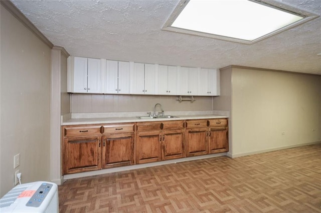 kitchen featuring a sink, light countertops, white cabinets, a textured ceiling, and brown cabinets