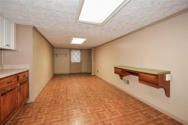 finished below grade area featuring visible vents, baseboards, a textured ceiling, and ornamental molding