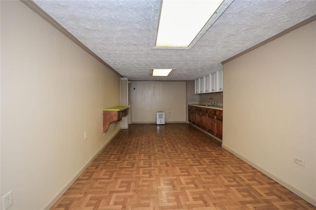 finished below grade area with a textured ceiling, ornamental molding, baseboards, and a sink