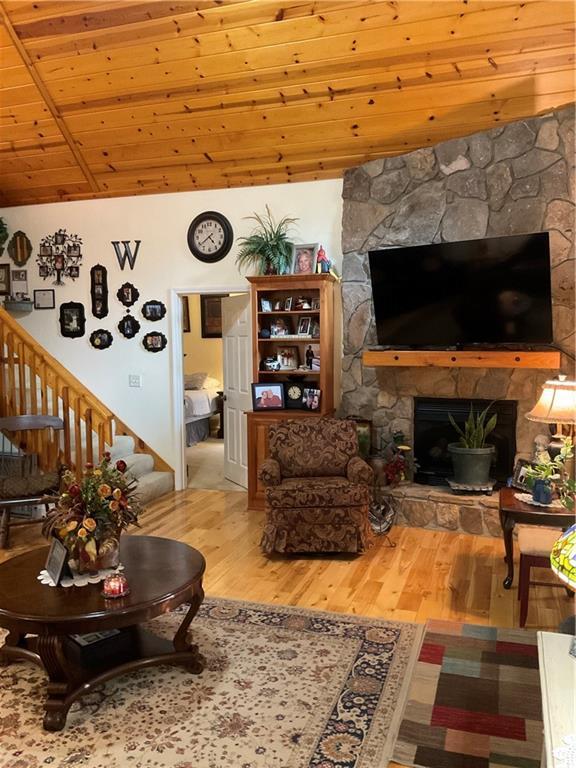 living room with stairway, wood finished floors, lofted ceiling, a fireplace, and wood ceiling