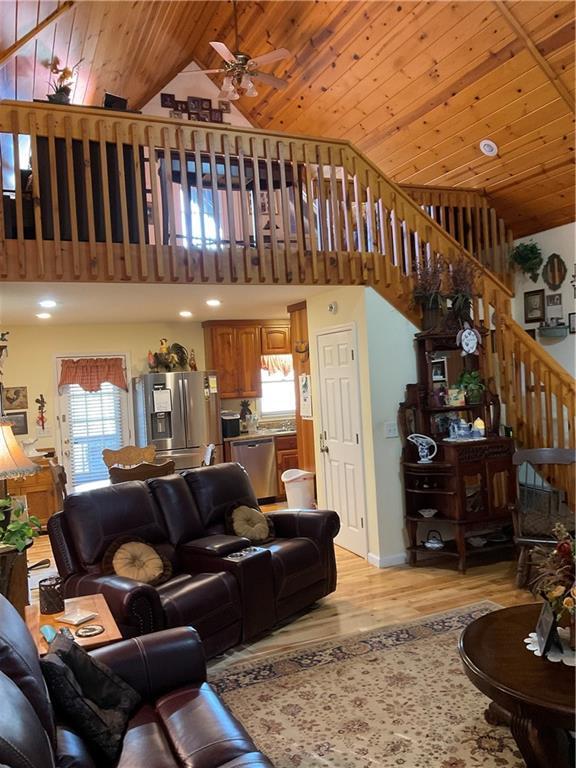 living area featuring high vaulted ceiling, ceiling fan, stairs, wooden ceiling, and light wood-type flooring