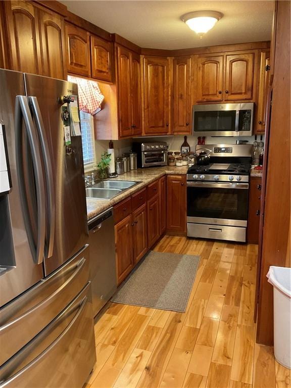 kitchen with a sink, brown cabinets, appliances with stainless steel finishes, and light wood-style flooring