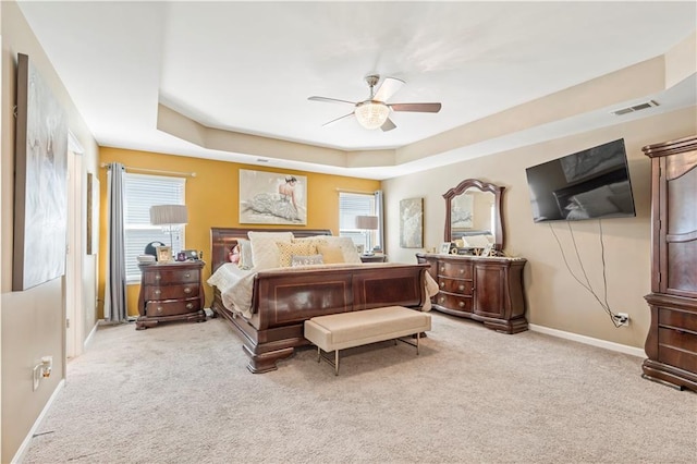 bedroom with ceiling fan, light carpet, visible vents, baseboards, and a raised ceiling