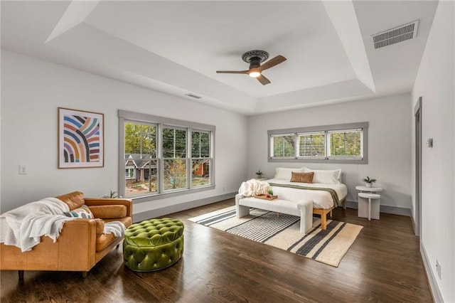 bedroom featuring a tray ceiling, multiple windows, visible vents, and wood finished floors