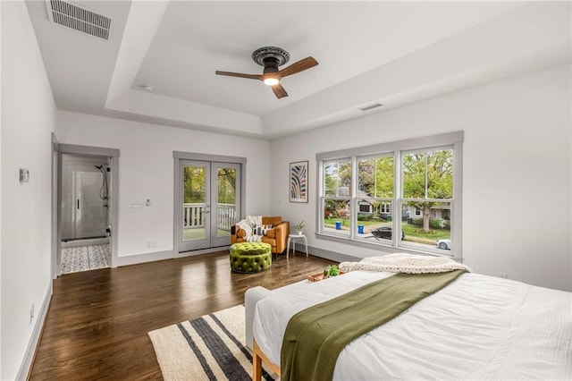 bedroom with access to outside, a tray ceiling, visible vents, and wood finished floors