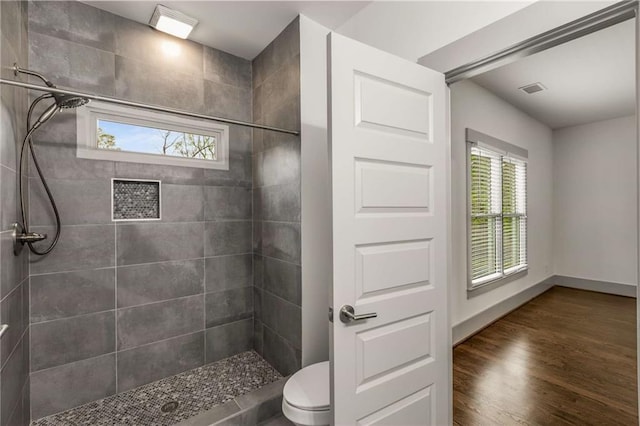 full bathroom featuring wood finished floors, baseboards, a tile shower, and a wealth of natural light
