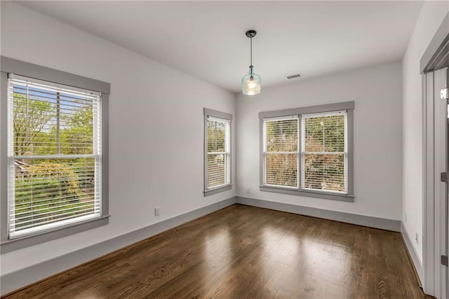 spare room featuring visible vents, plenty of natural light, baseboards, and wood finished floors
