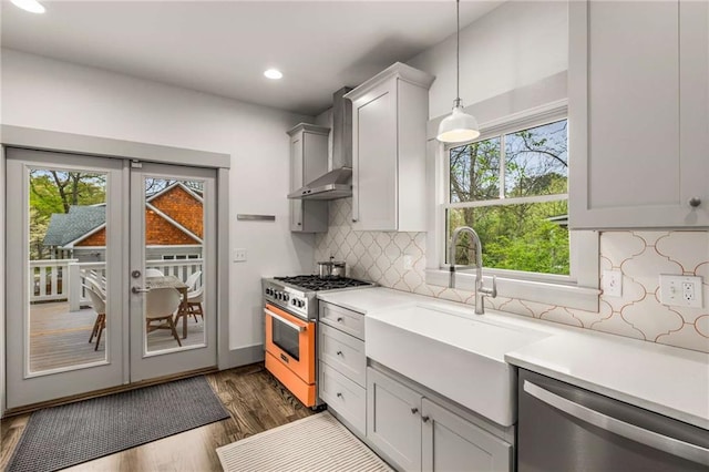 kitchen featuring light countertops, stainless steel appliances, a sink, wall chimney range hood, and french doors