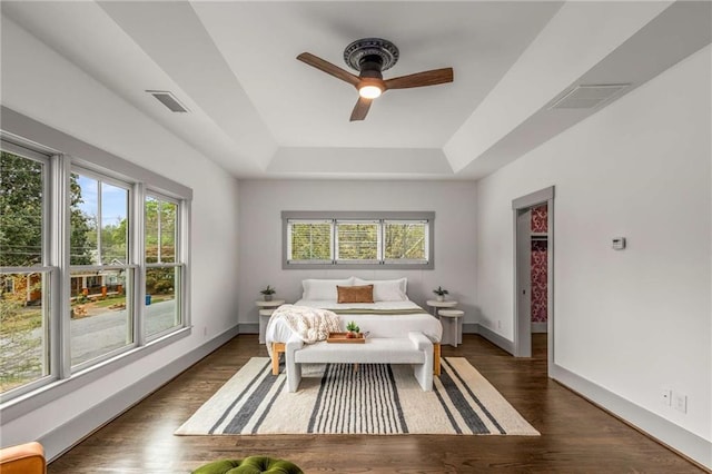 bedroom featuring a tray ceiling, visible vents, multiple windows, and wood finished floors