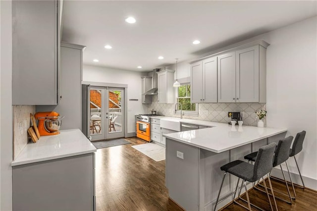 kitchen featuring dark wood finished floors, a sink, stainless steel range, wall chimney range hood, and gray cabinets