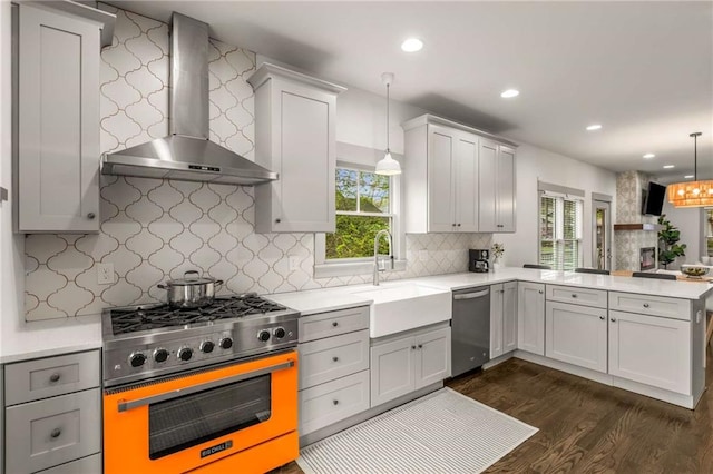 kitchen featuring a peninsula, wall chimney exhaust hood, stainless steel appliances, dark wood finished floors, and a sink