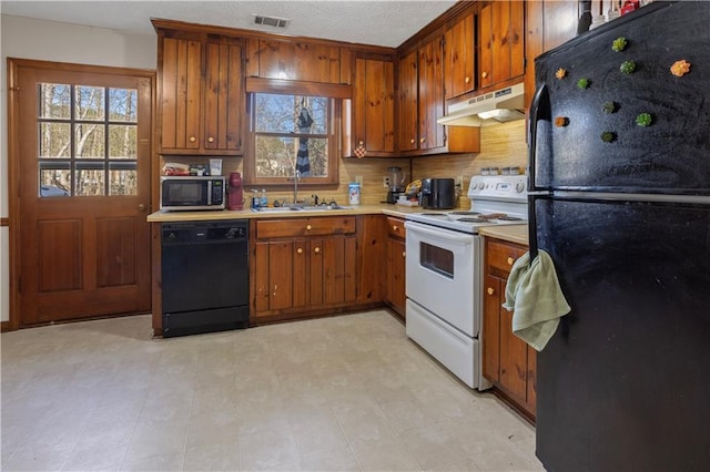 kitchen featuring under cabinet range hood, a sink, visible vents, light countertops, and black appliances