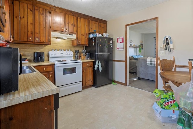 kitchen with electric stove, brown cabinets, freestanding refrigerator, light countertops, and under cabinet range hood