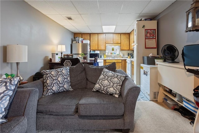 living area with a paneled ceiling, visible vents, and light colored carpet