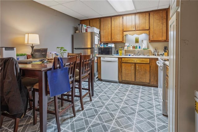 kitchen featuring light floors, light countertops, brown cabinetry, a sink, and white appliances