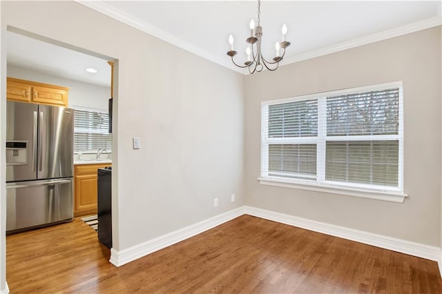 unfurnished dining area with sink, ornamental molding, light hardwood / wood-style floors, and an inviting chandelier