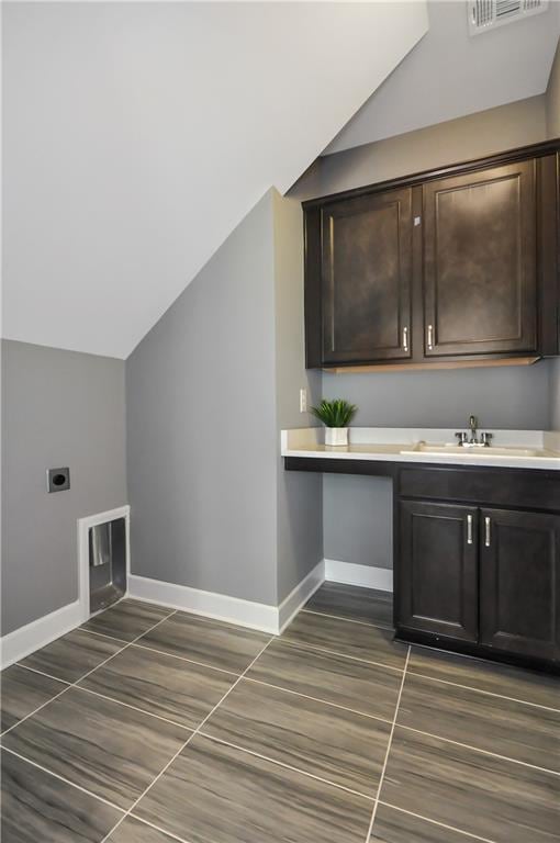 washroom featuring electric dryer hookup, baseboards, cabinet space, and dark tile patterned flooring