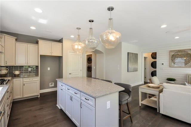 kitchen featuring dark wood-style floors, baseboards, a breakfast bar, light stone countertops, and a kitchen island