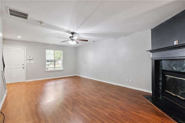 unfurnished living room with ceiling fan, a premium fireplace, wood finished floors, and baseboards
