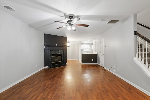 unfurnished living room with a ceiling fan, dark wood-type flooring, stairs, a fireplace, and baseboards