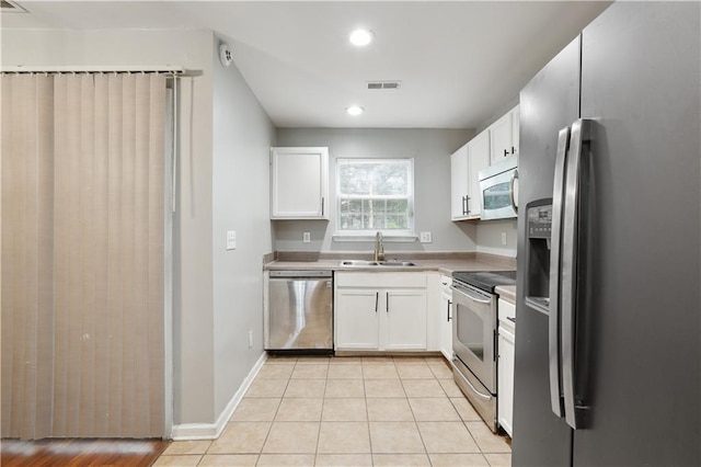 kitchen with appliances with stainless steel finishes, a sink, white cabinets, light tile patterned floors, and recessed lighting
