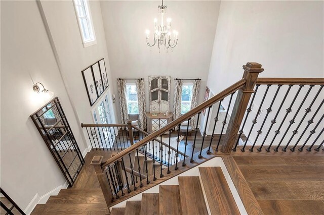 staircase featuring a towering ceiling, wood-type flooring, and an inviting chandelier