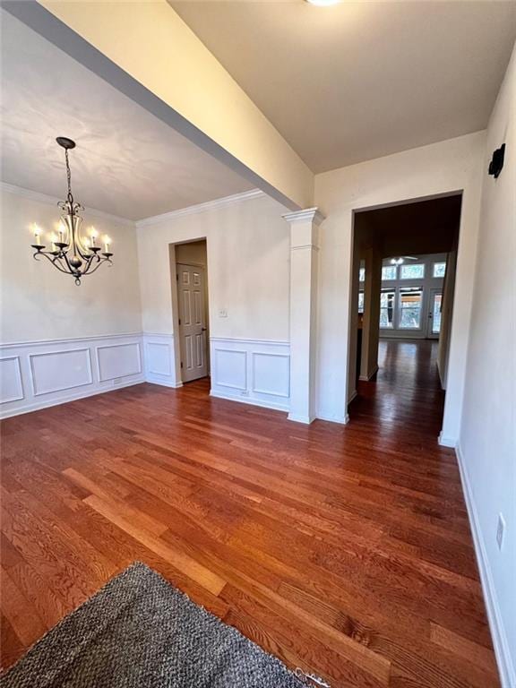 spare room featuring dark wood-type flooring, crown molding, an inviting chandelier, and decorative columns