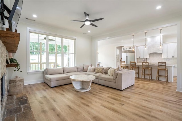 living room with sink, a fireplace, light hardwood / wood-style floors, ceiling fan, and crown molding