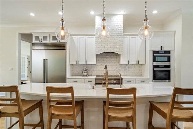 kitchen with backsplash, appliances with stainless steel finishes, a kitchen breakfast bar, white cabinetry, and an island with sink