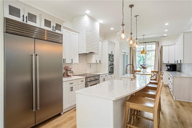 kitchen with sink, high quality appliances, backsplash, white cabinets, and a center island with sink