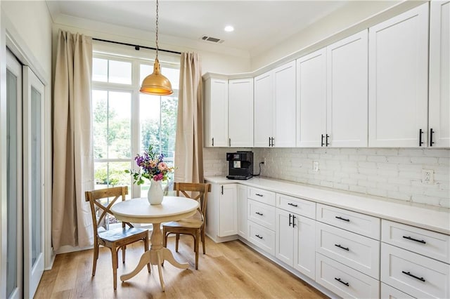 kitchen featuring crown molding, white cabinets, hanging light fixtures, and light wood-type flooring