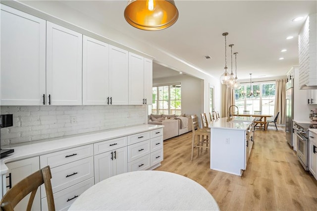 kitchen with hanging light fixtures, white cabinetry, a kitchen island with sink, light hardwood / wood-style floors, and high end appliances