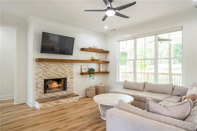 living room featuring ornamental molding, a fireplace, light wood-type flooring, and ceiling fan